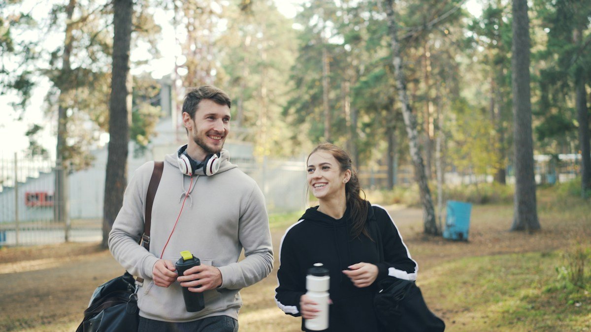 Two people carrying gym bags and drink bottles outdoors